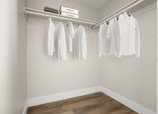 a walk in closet with white clothes hanging on a rail